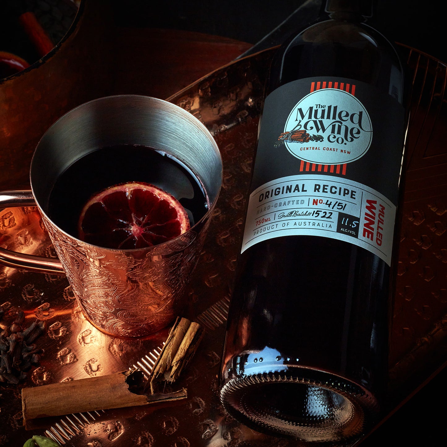 Bottle of Australian mulled wine next to a copper cup with orange slice garnish.